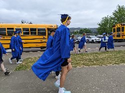 Students in graduation robes walk by buses